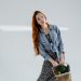 Young woman in denim shirt posing with eco-friendly basket of vegetables in a bright studio.
