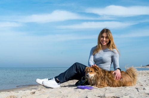 Woman enjoying a sunny day on Kołobrzeg beach with her dog, capturing the essence of leisure and companionship.